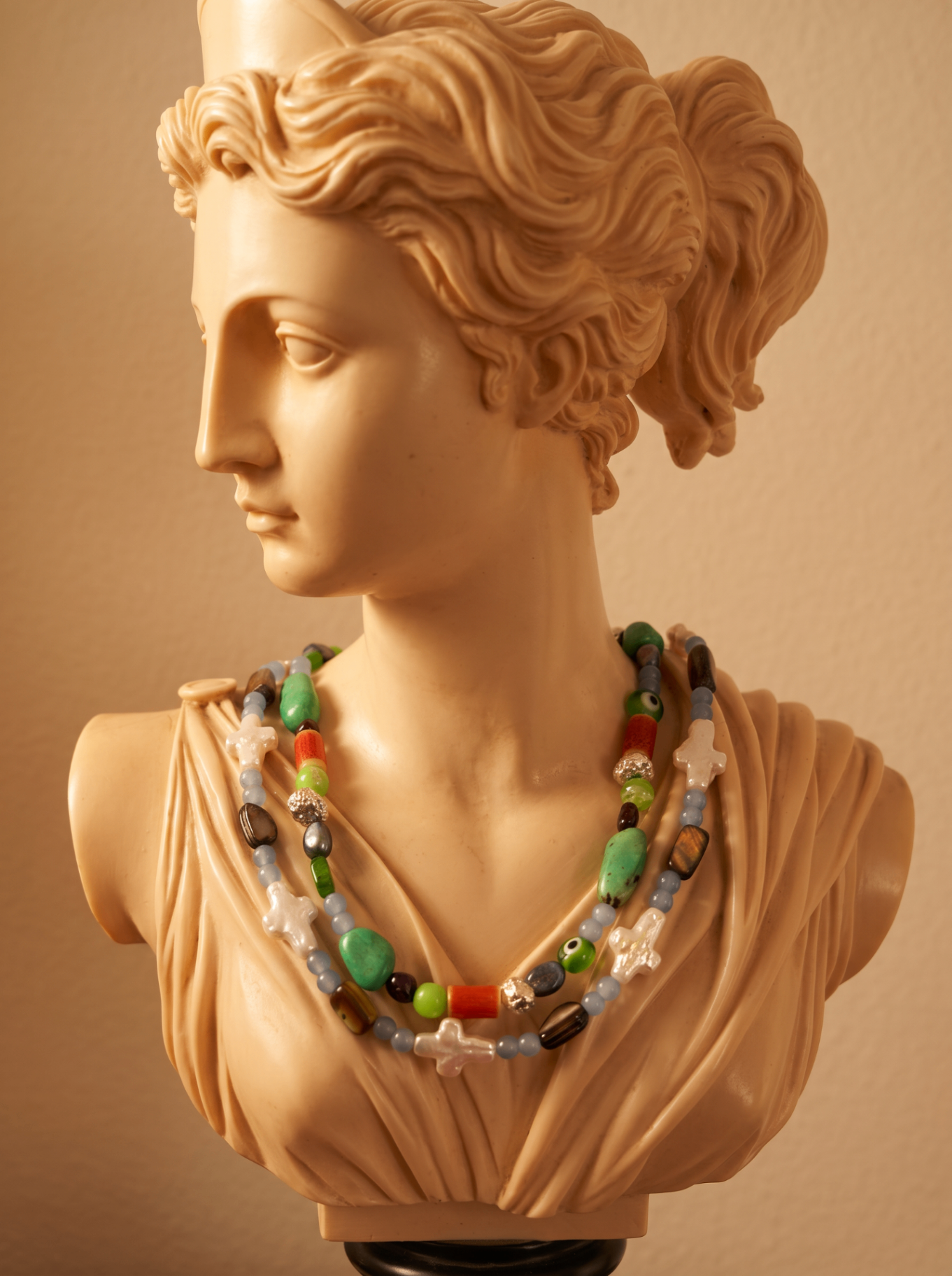 A neoclassical bust wearing layered beaded necklaces of turquoise, coral, pearl crosses, and glass beads